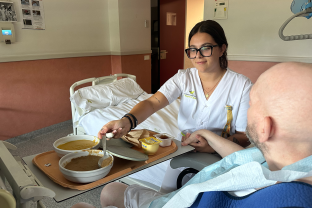 Una Técnica en Cuidados Auxiliares de Enfermería dando de comer a un paciente.